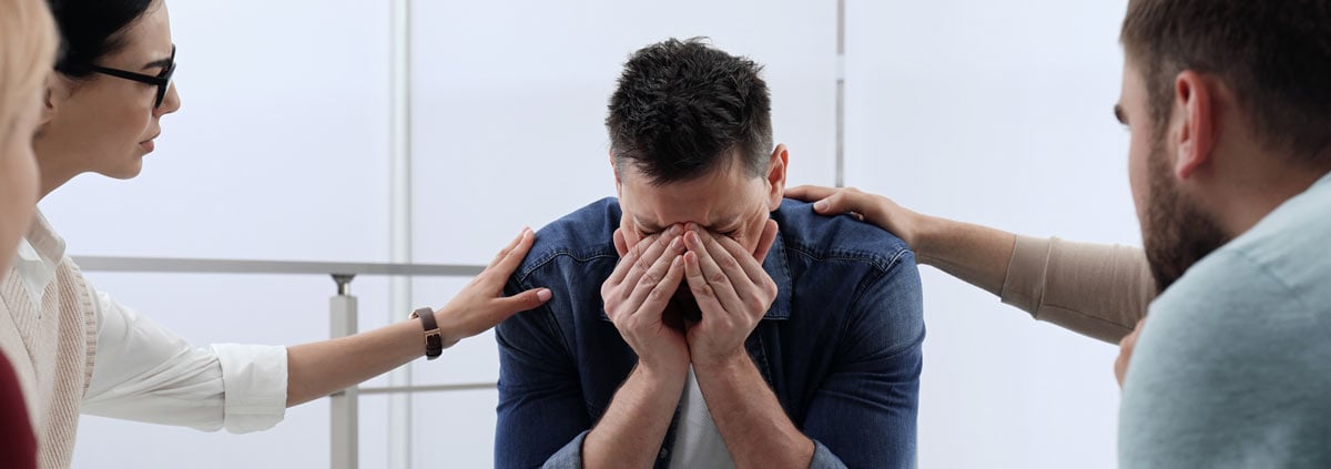 Upset man being consoled in group therapy